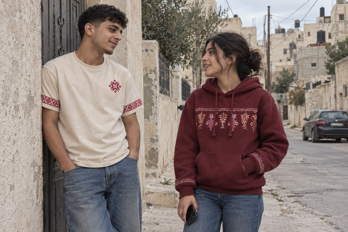 Man wearing the cream tatreez star and sleeve T-shirt, chatting with a woman in a burgundy hoodie outdoors.