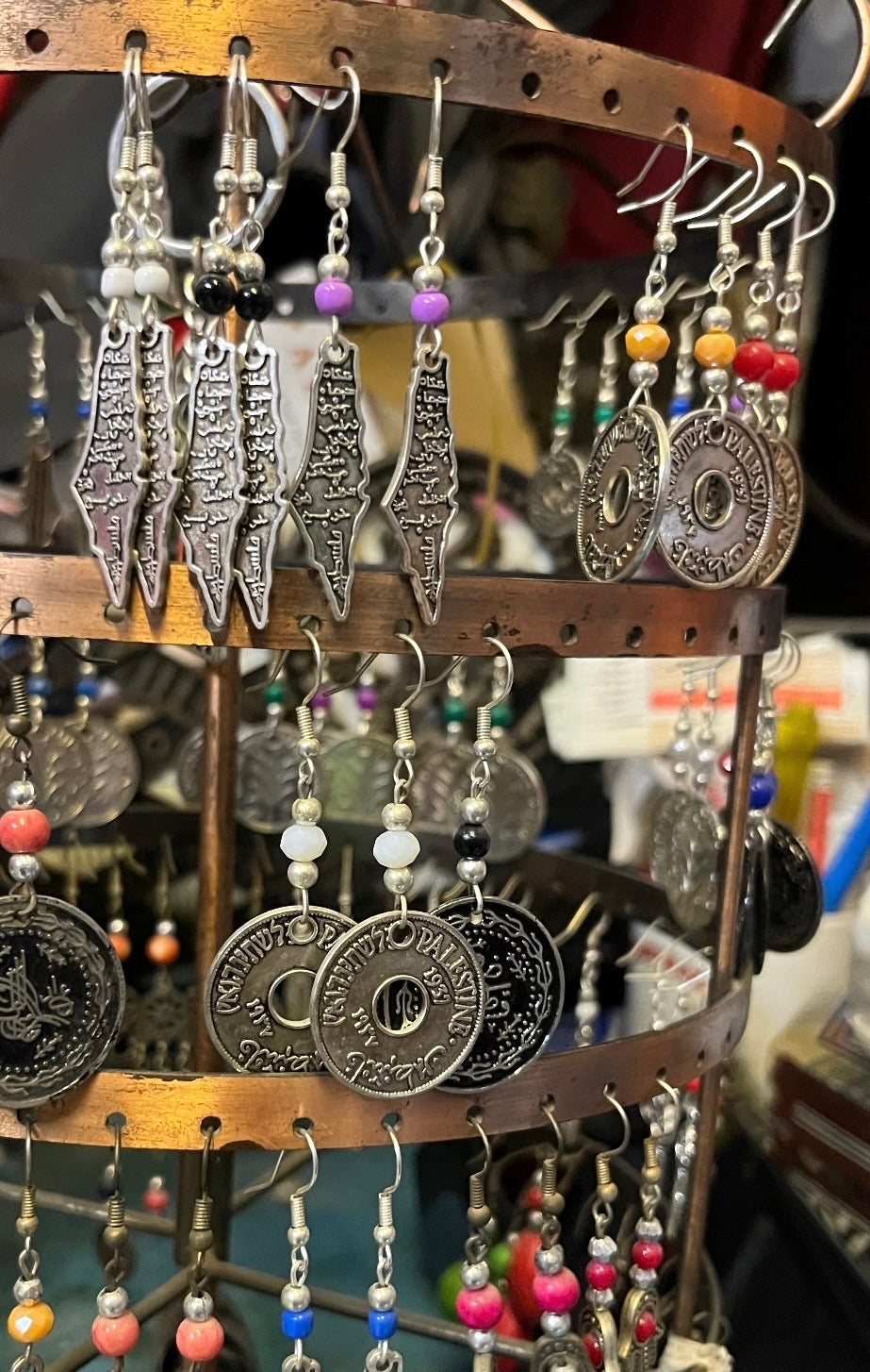 Palestine map and coin earrings with coloured beads displayed on a rack in the Bethlehem shop