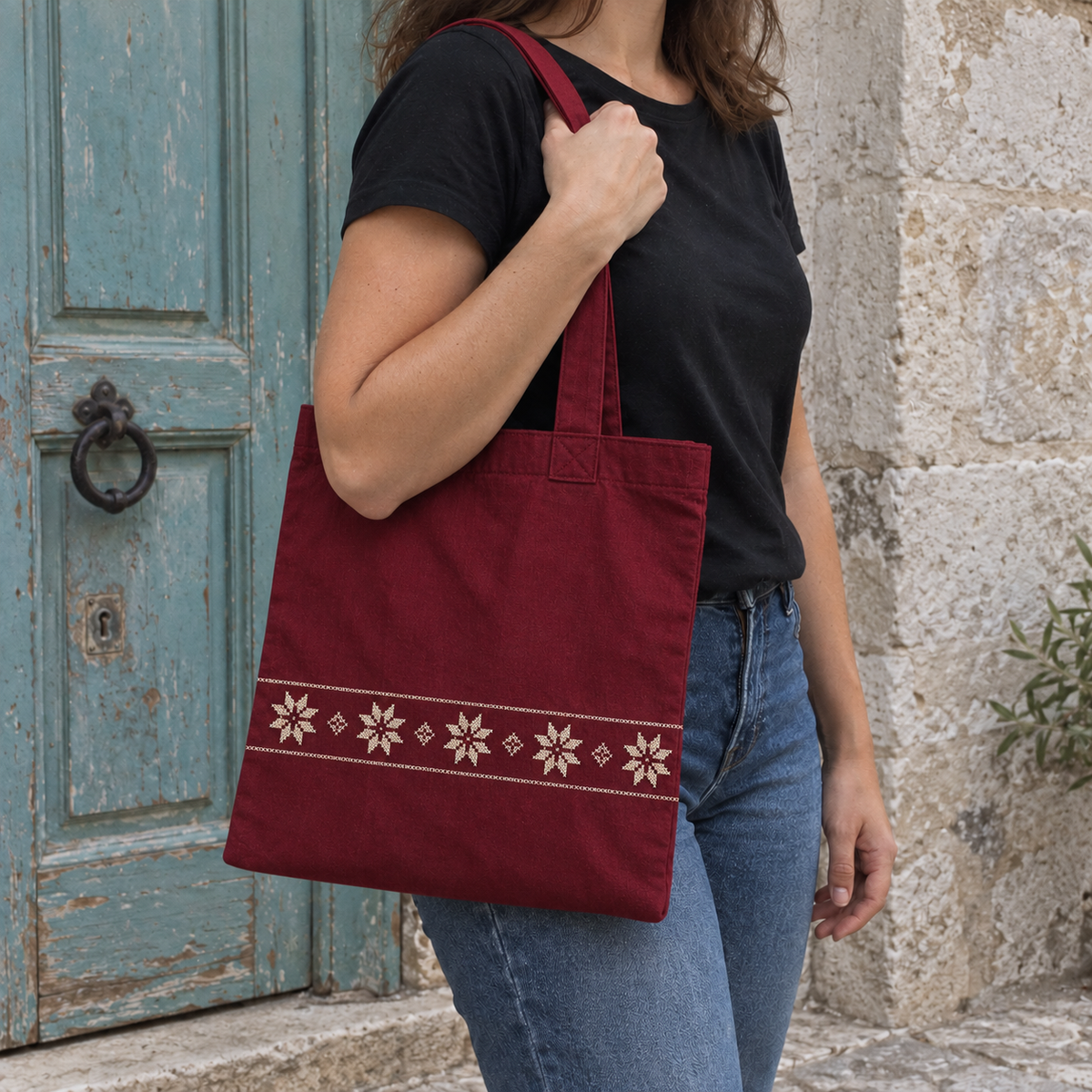 Burgundy star-border tote worn over the shoulder beside a turquoise door
