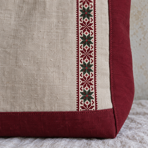 Fine burgundy ivory and green tatreez stitches on oatmeal linen beside the burgundy base and side seam