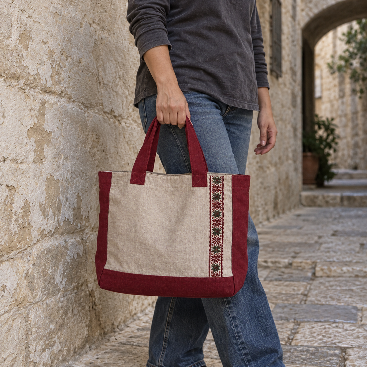 Oatmeal linen tote with burgundy trim and vertical tatreez carried by its burgundy handles