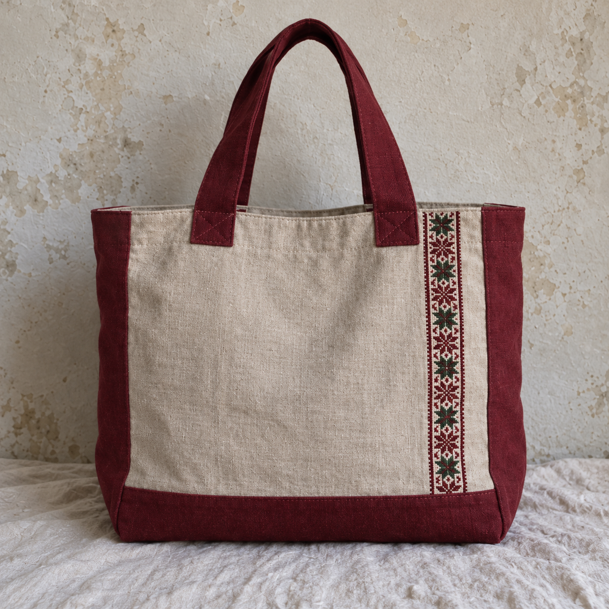 Oatmeal linen carryall with burgundy sides handles and base and a vertical tatreez band