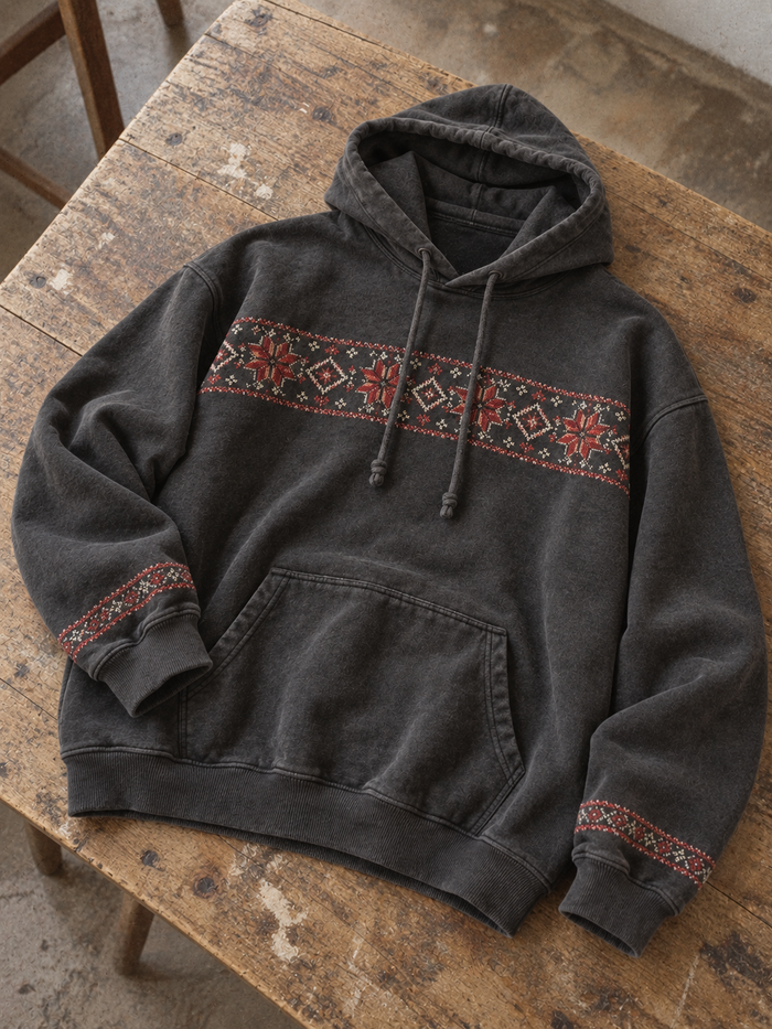 Charcoal hoodie laid on a wooden table, with red and cream tatreez across the chest and cuffs.