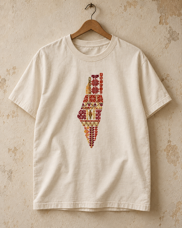 Cream Palestine motifs tatreez map T-shirt hanging against a plaster wall.