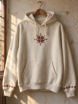 Cream hoodie on a wooden hanger with burgundy tatreez chest star and embroidered cuffs.