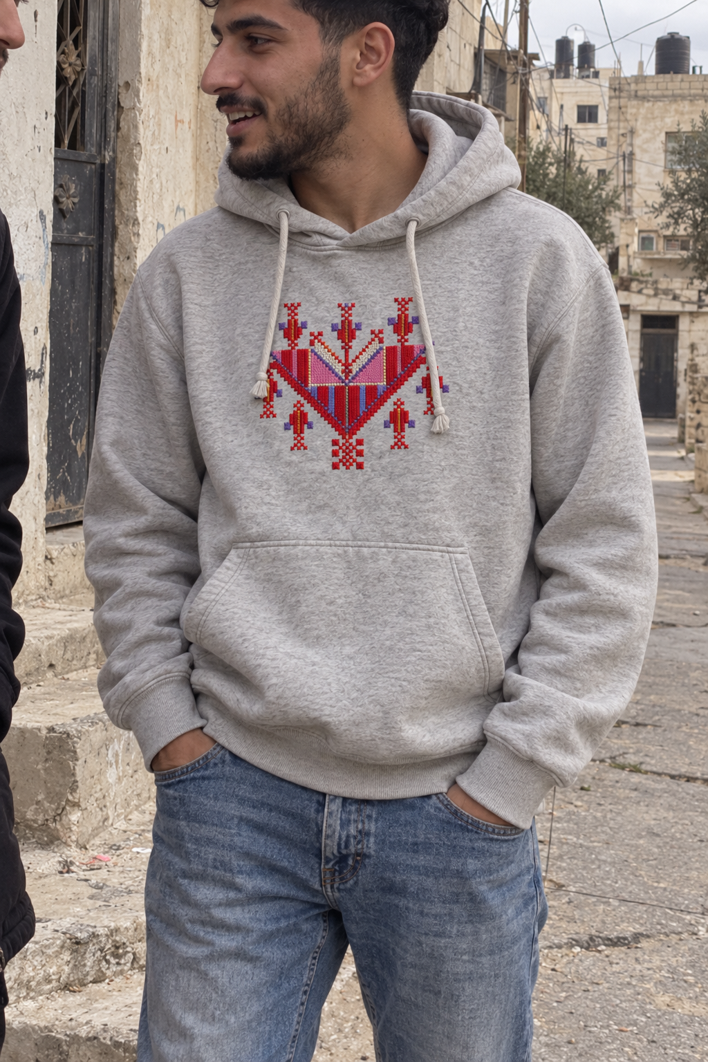 Man wearing a light-grey hoodie with colourful Gaza-inspired tatreez chest embroidery.