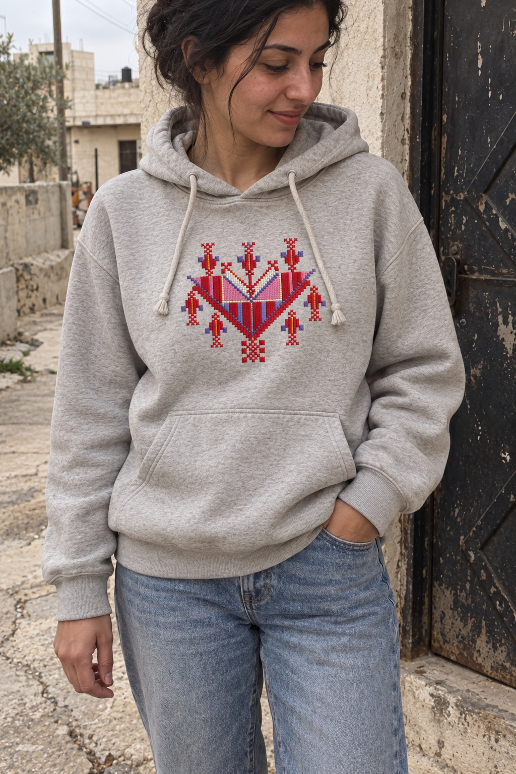 Woman wearing a light-grey hoodie with colourful Gaza-inspired tatreez chest embroidery.