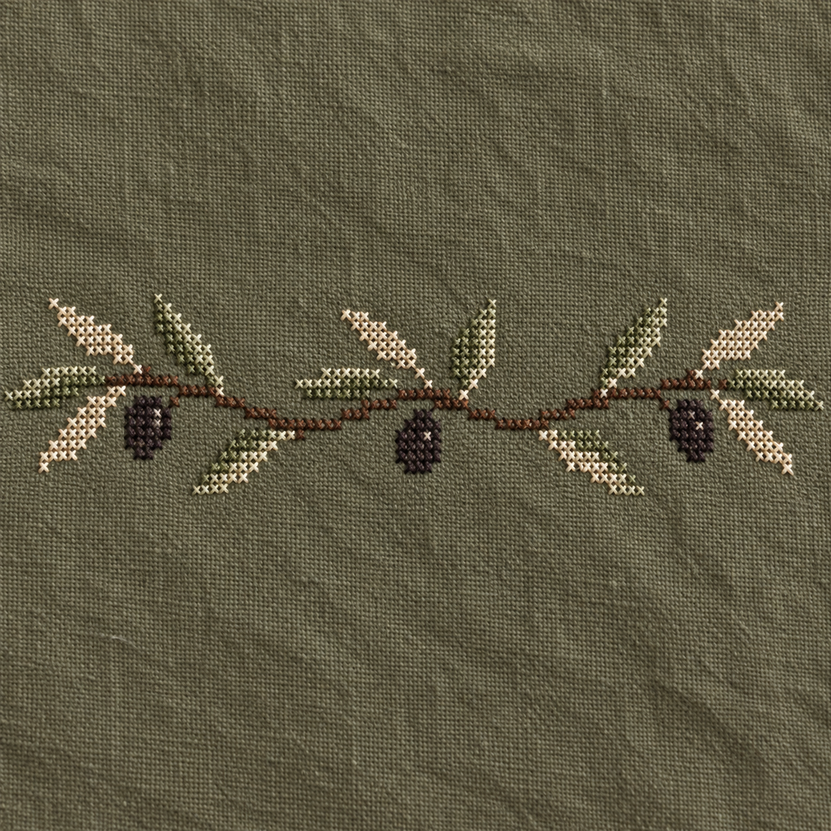 Close-up of ivory and sage olive leaves and three dark olives worked in fine cross stitches