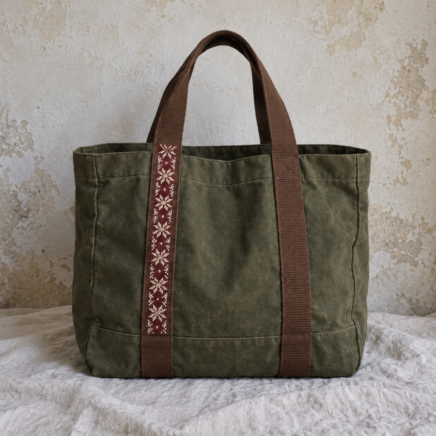 Olive canvas market tote with tatreez along one brown webbing strap