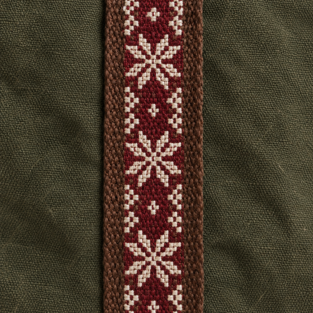 Close-up of burgundy and ivory tatreez stitched over brown webbing on olive cotton canvas