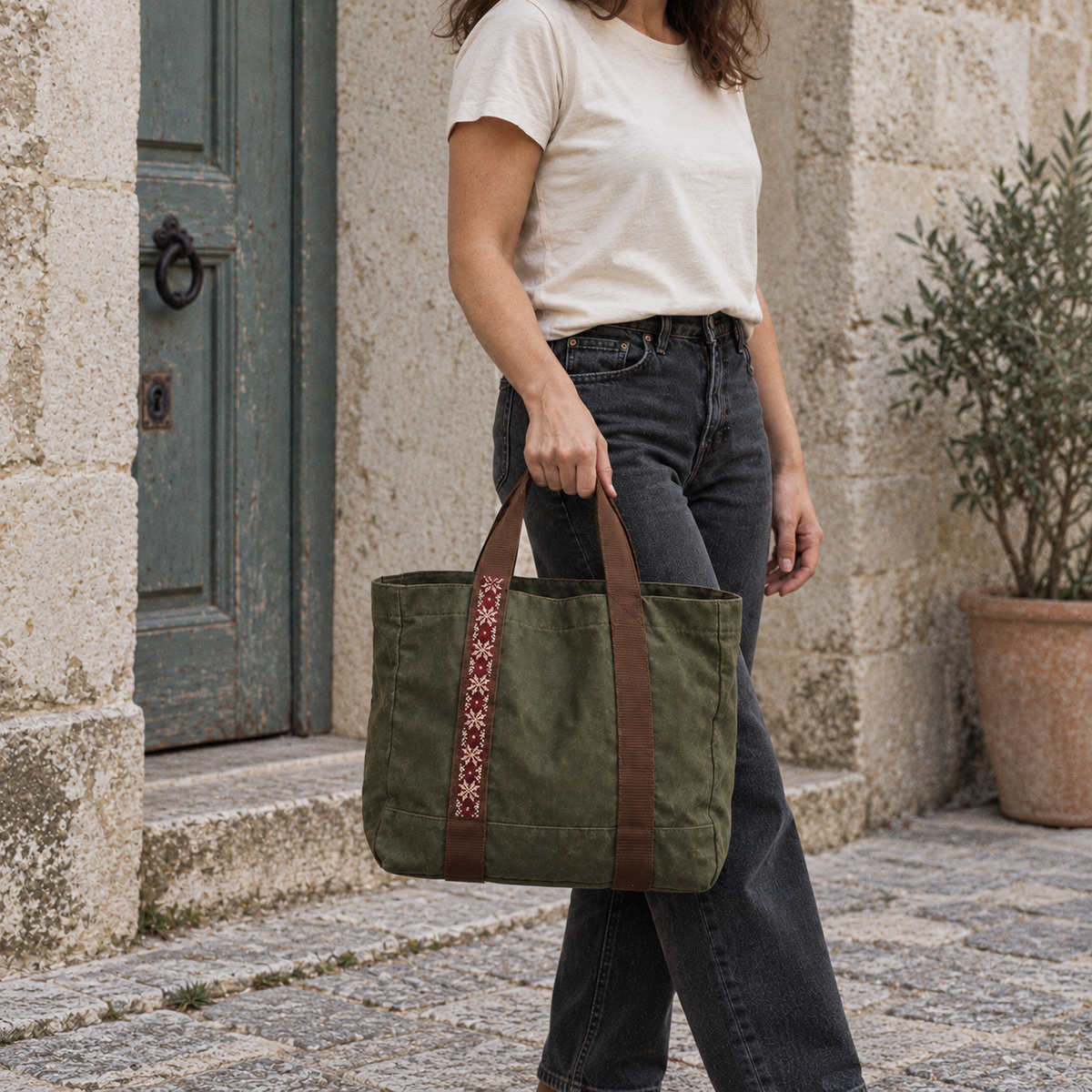 Olive canvas tatreez market tote carried by hand beside a turquoise door