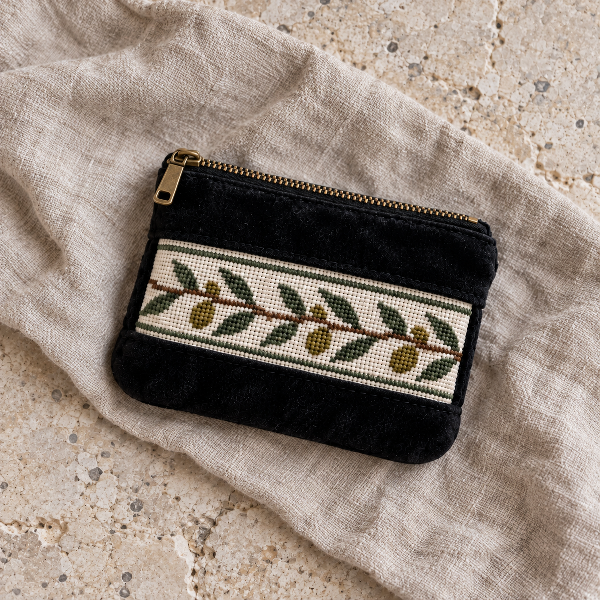 Black velvet olive tatreez coin purse lying on neutral linen