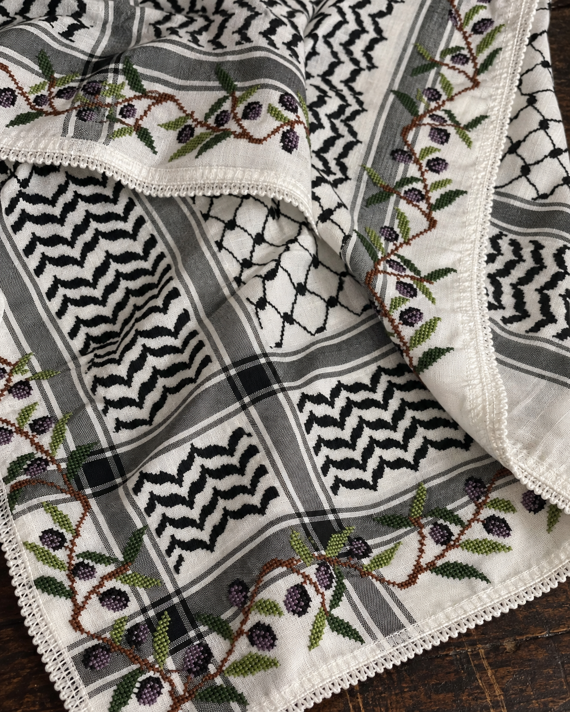 AI-assisted close-up of green leaves, brown branches and dark olives embroidered along the keffiyeh border.