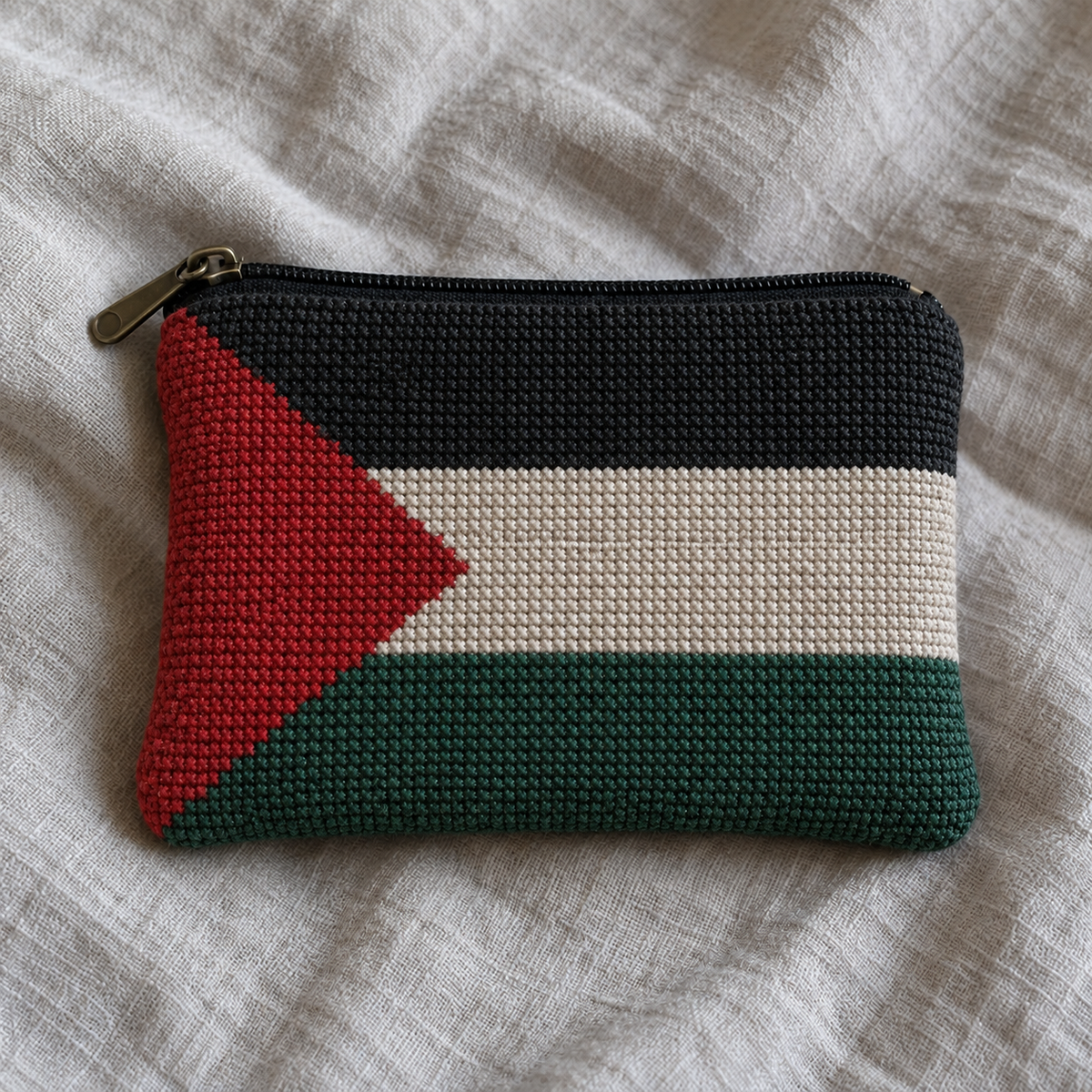 Coin purse covered in Palestinian flag cross-stitch embroidery with a black zip and brass-coloured pull