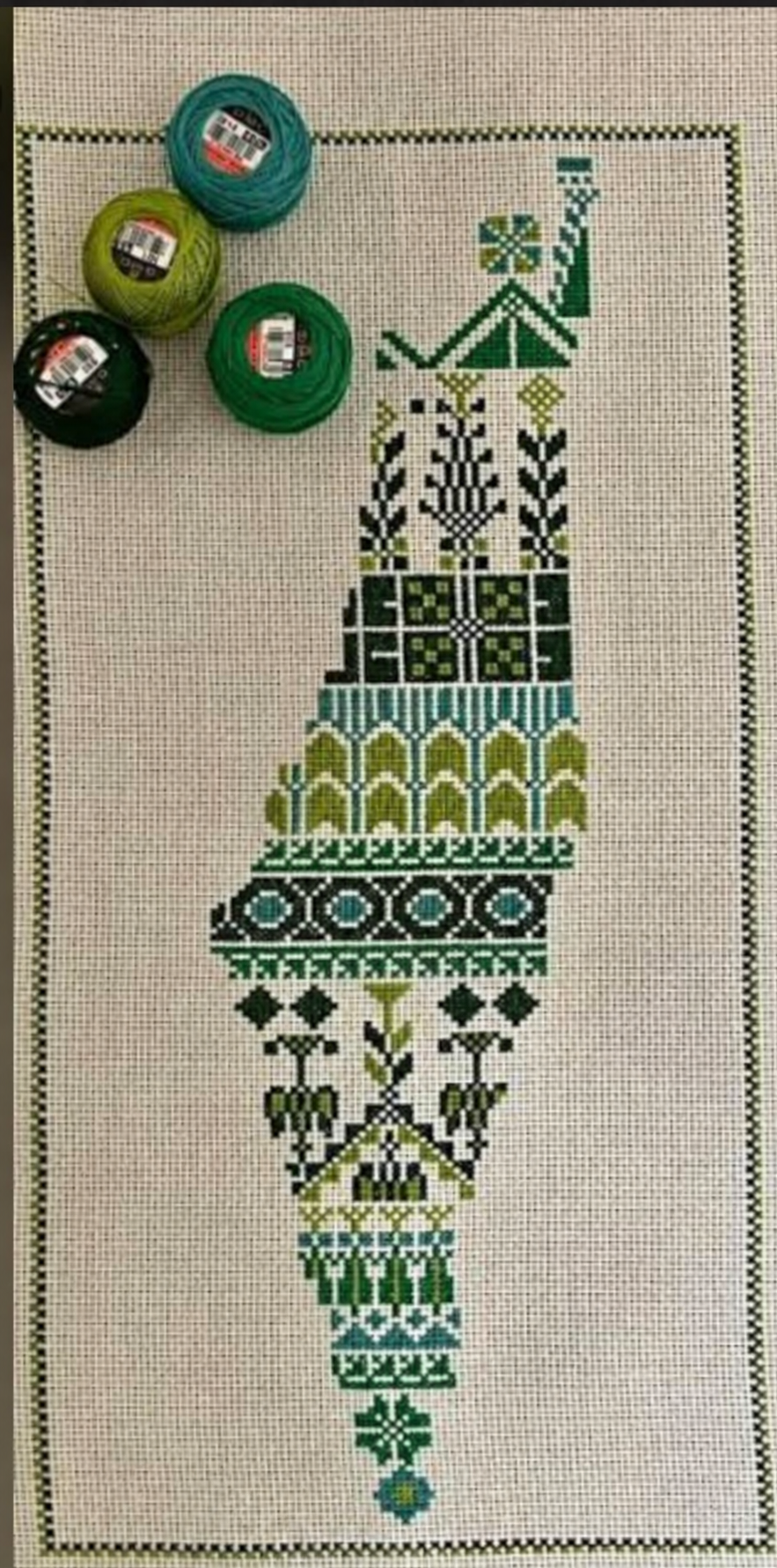 Green and olive geometric tatreez Palestine map on Aida cloth beside embroidery threads