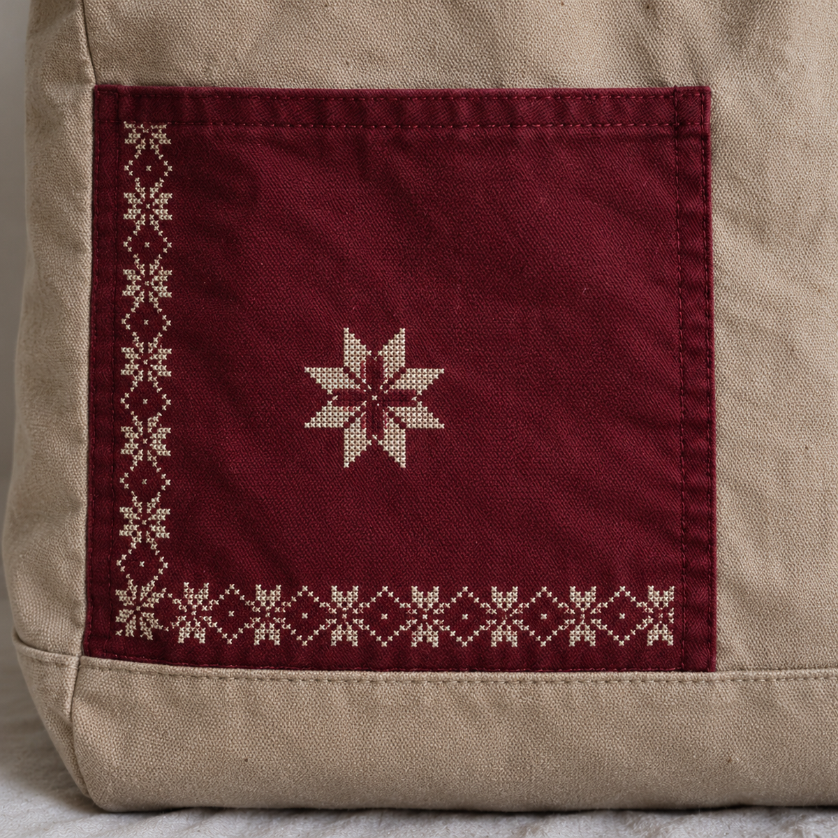 Close-up of ivory star tatreez and border on the burgundy pocket of a sand canvas tote
