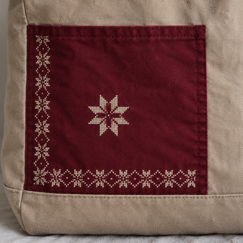 Close-up of ivory star tatreez and border on the burgundy pocket of a sand canvas tote
