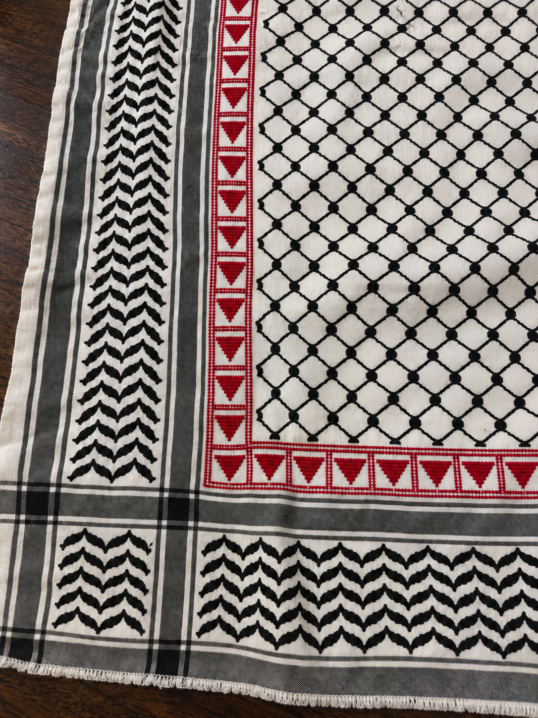 Close-up of filled red triangle tatreez and traditional black woven keffiyeh borders